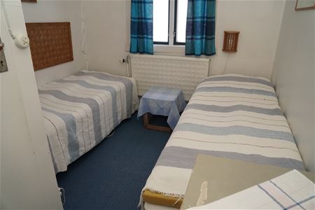 Two beds on each side of a window with blue checkerd curtains.