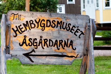 Träskylt med text till hembygdsmuseet Åsgårdarna.