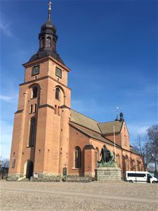 Kristine kyrka i rött tegel, framför kyrkan en staty av Engelbrekt och en vit minibuss.