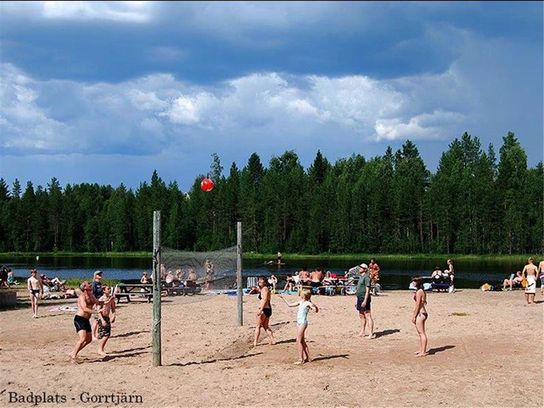Beach volleyball is played on a sandy beach by a small lake.