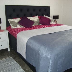 Dubbelsäng med mörkgrå, stoppad sänggavel och en sänglampa på en byrå bredvid sängen. 