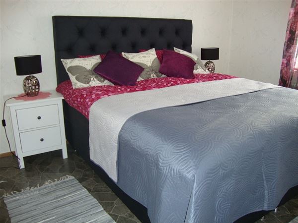 Dubbelsäng med mörkgrå, stoppad sänggavel och en sänglampa på en byrå bredvid sängen.  