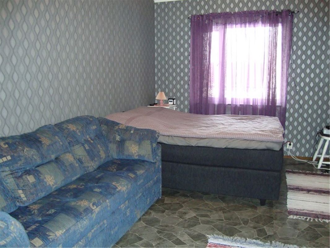Blue patterned sofa and a bed placed in front of a window vith thin, violet curtains. 