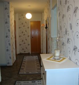 Hall med vit byrå, med ljuslykta och ljusgrå mattor på ett mörkgrått golv. 
