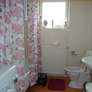Badrum med toalett, handfat och ett badkar bakom ett rosa-blommigt duschdraperi. 