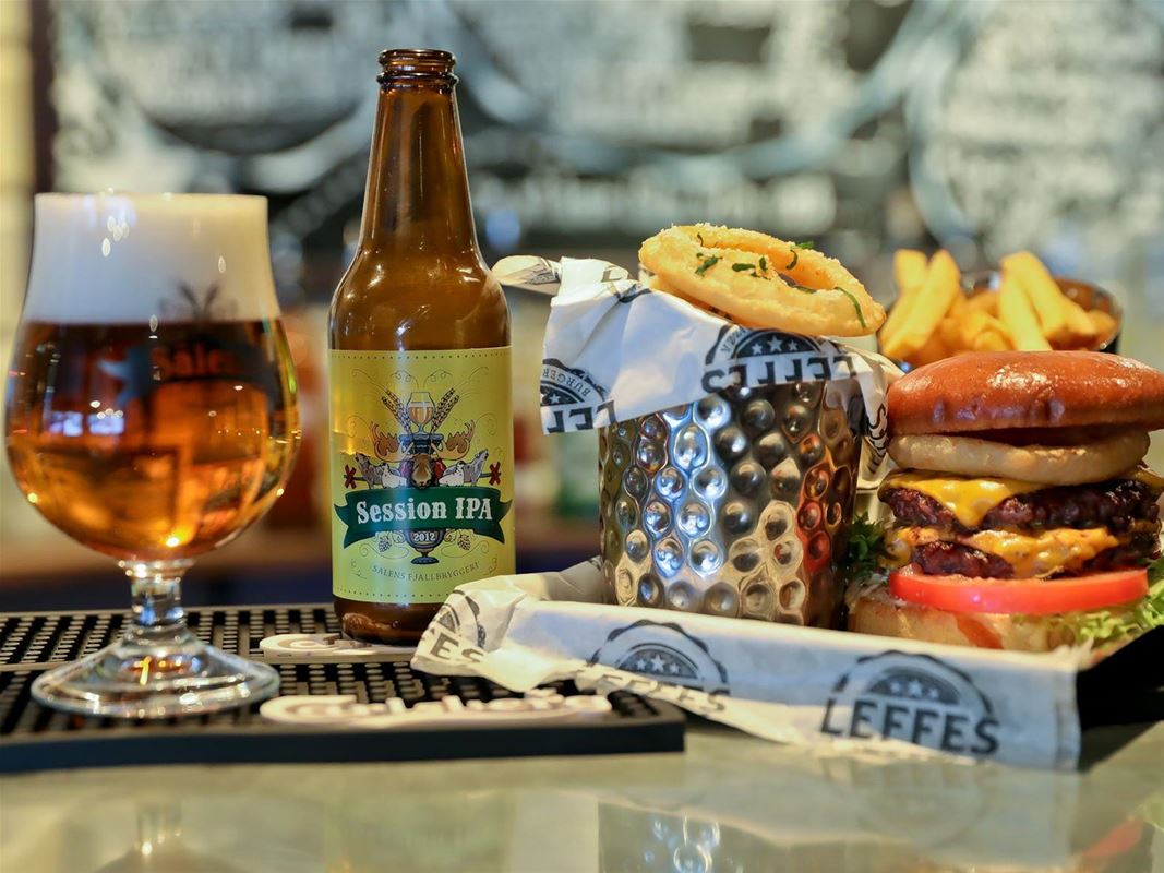 En bricka med hamburgare och ett glas öl bredvid en flaska. 