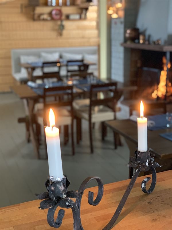 Ljusstake med två brinnande ljus på ett bord. Det brinner en eld i öppna spisen i bakgrunden. 