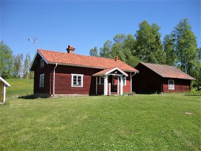 Red log cabin with a smaller cottage beside on a large green lawn. 