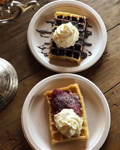 Two plates with waffles, jam and cream.