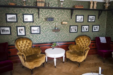 Salongen med två rokokofåtöljer klädda i senapsgul sammet och ett vitt runnt bord. Svartvita bilder på väggen.