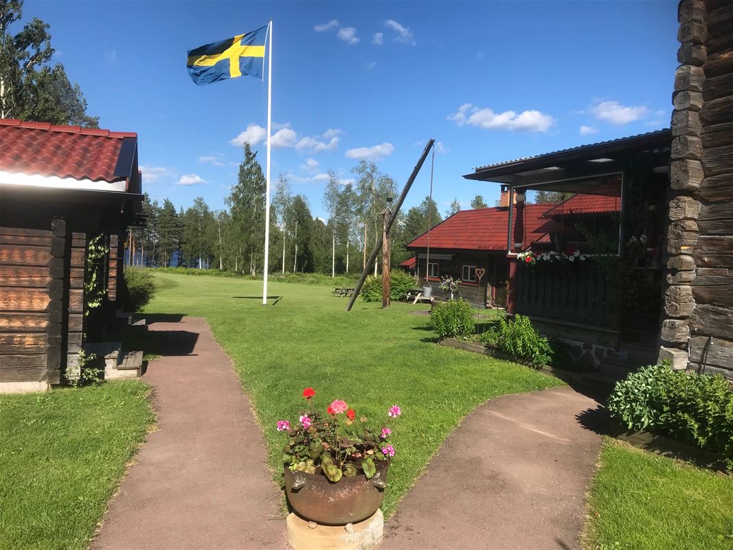 Flowers in a flowerpot in front of a flagpole with a swedish flag blowing in the wind. 