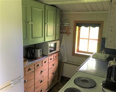 Small pentry with bureau and cupboards on the wall on one side and stove and sink on the other side of a small window.