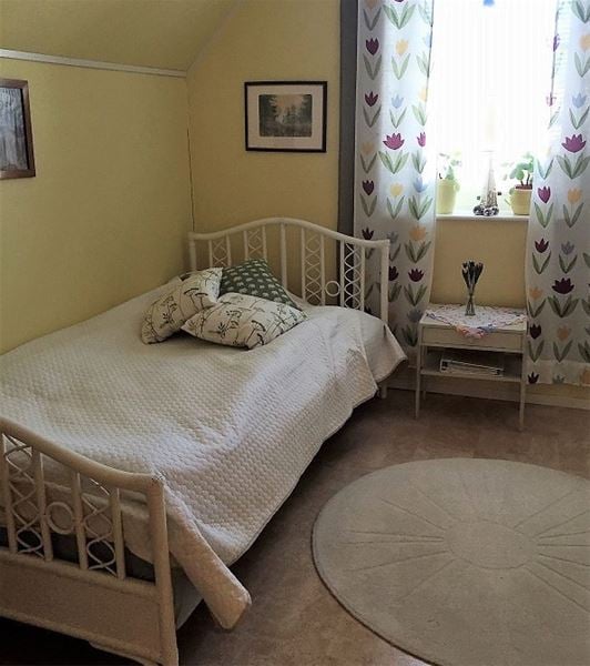 Enkelsäng i vit sängram som står i ett gult rum med tulpaner på gardinerna.  