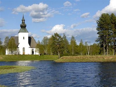 Exterior white church with streams in front and greenery around.