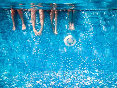 Underwater view of four people's legs in a pool with blue mosaic tiles