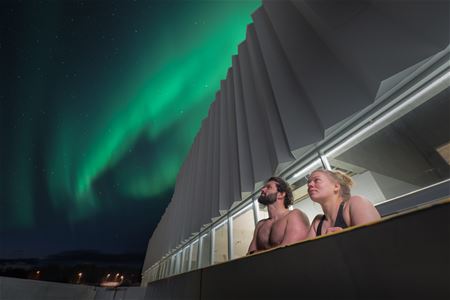 A man and a woman enjoying the Northern Lights from the pool