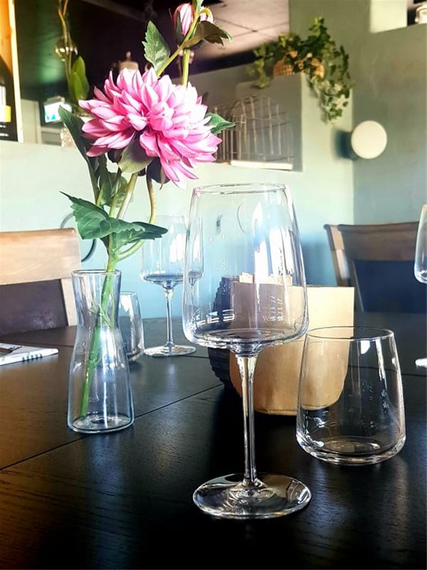 A wine glas and flower in vase on table.