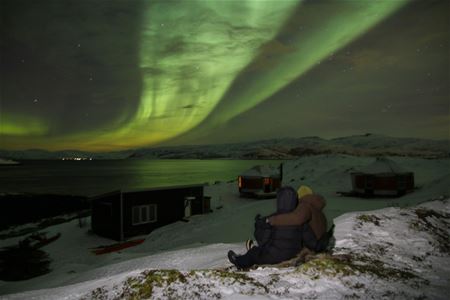 Mann og kvinne ser på nordlyset over havet