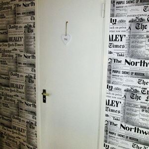 Toalettdörr i en hall med tapet som ser ut som gamla  dagstidningar.