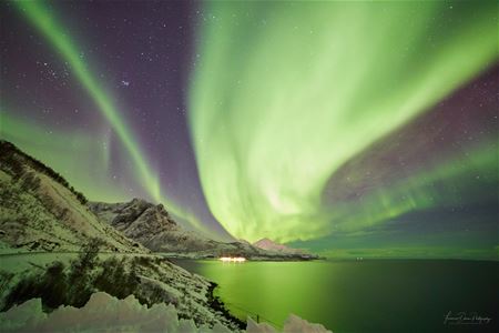 strong northern lights covering the whole sky over mountains and sea