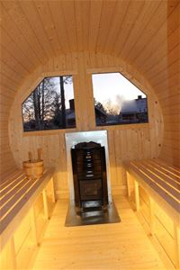 Sauna with a black stove in front of two large windows. 