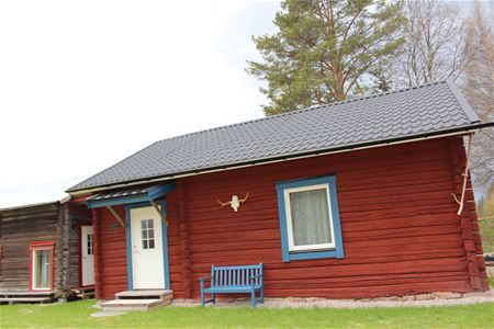 Red cabin with a blue bench in front of the cabin. 
