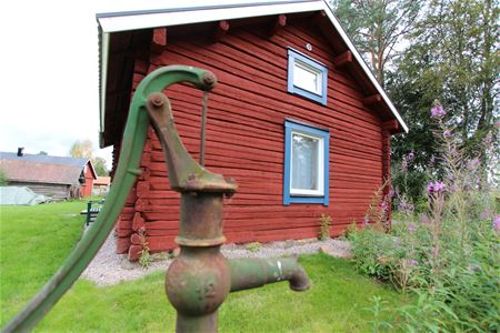 Water pump in front of a red log cabin.