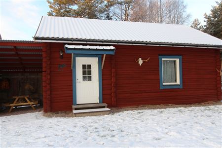 Red log cabin with snow on the roof. 