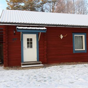 Red log cabin with snow on the roof. 