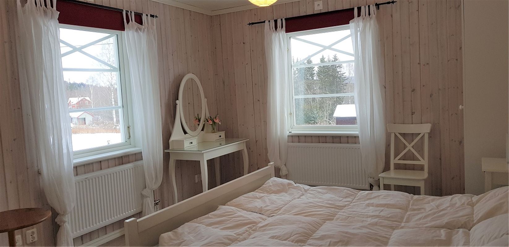 Bedroom with two windows and a dressing table in the corner.