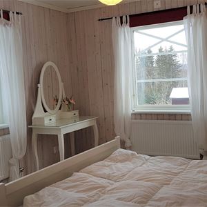 Sovrum med vit sängstomme, vit stol, vitt sminkbord och vita gardiner.