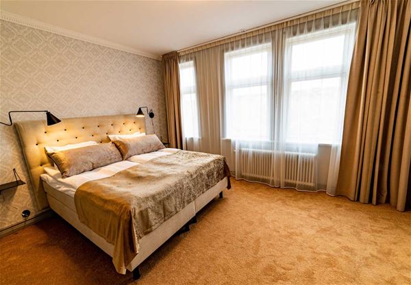 Dubbelrum med gyllenbruna färger på heltäckningsmatta, gardiner och sänggavel.  
