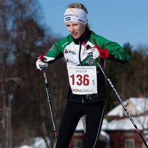 En tjej i svart, vit och grön klubbdräkt som åker längdskidor, nummerlapp med nummer 136 på magen.