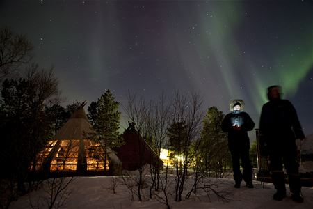 Gjester står utenfor gammen og ser på nordlyset