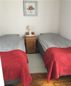 Dubbelrum med ljusa tapeter och två enkelsängar med ett sängbord i mitten.