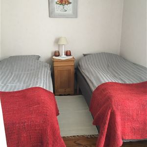 Dubbelrum med ljusa tapeter och två enkelsängar med ett sängbord i mitten.