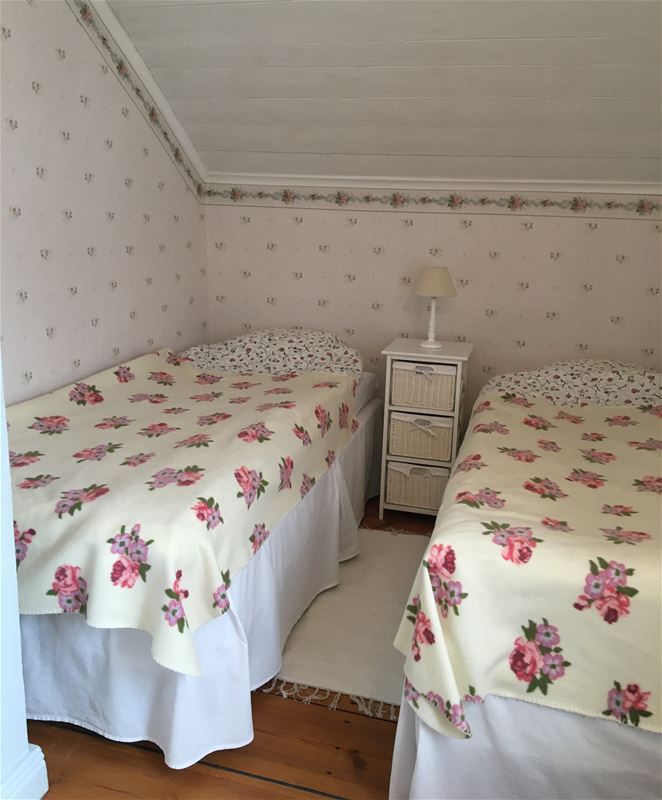 Bedroom with floral wallpaper and two single beds with a bedside table in between.