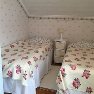 Dubbelrum med blommiga tapeter och två enkelsängar med ett sängbord i mitten.
