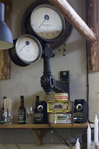 A wooden shelf with old tin cans, speakers, glasses and bottles.