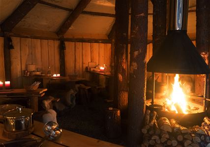 Circular wooden room with a central fireplace and benches covered in animal hides.