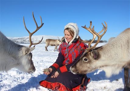 Person in traditional clothing with reindeer in snowy landscape.