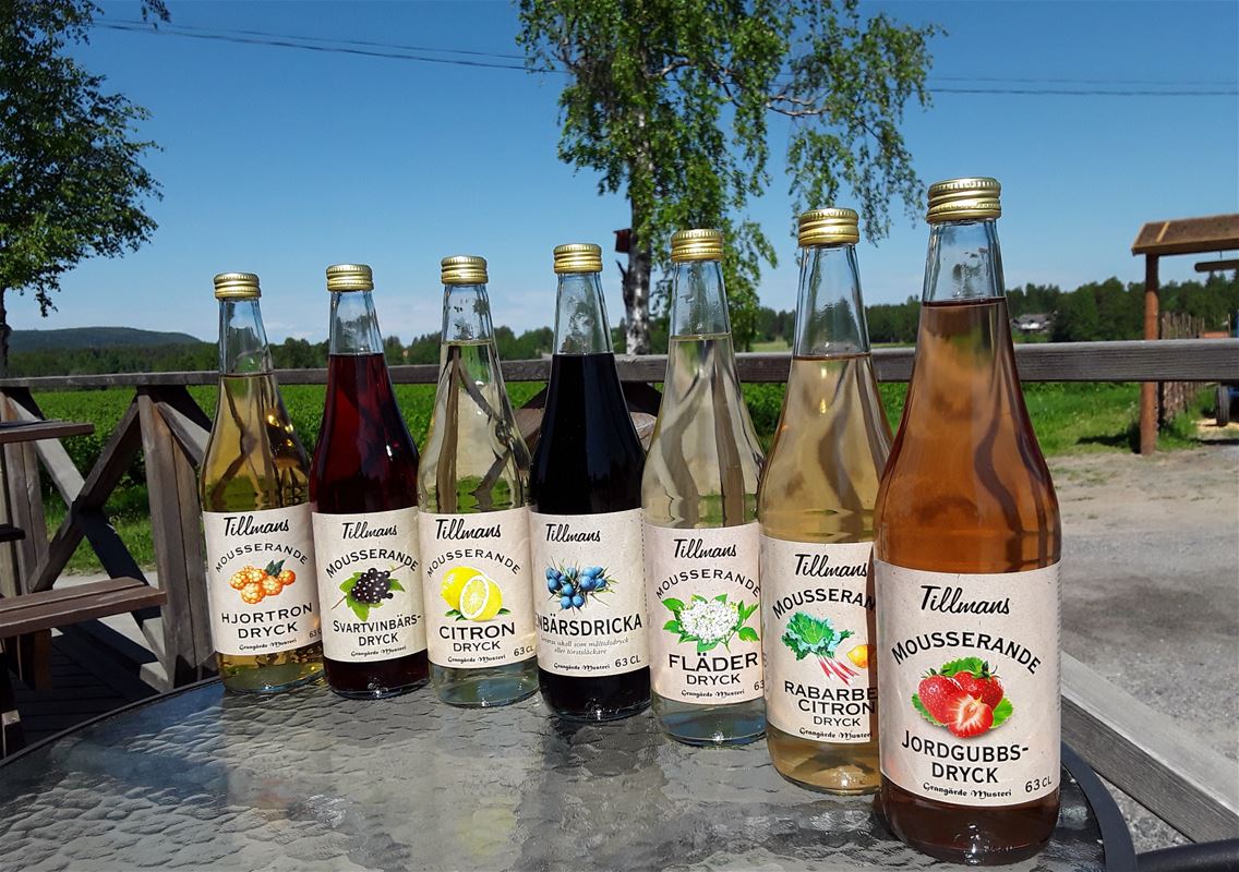 7 stycken flaskor på rad som innehåller olika slags fruktdrycker.