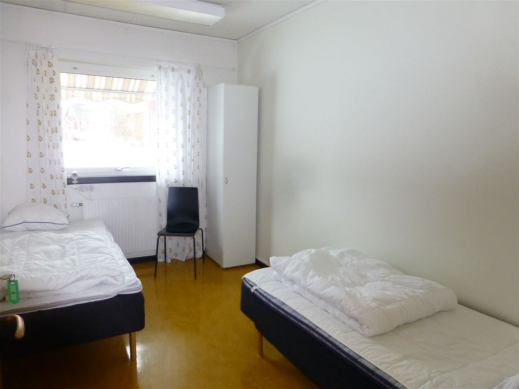 Rum med två enkelsängar på vardera sidan av rummet med ett fönster.