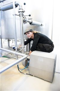 Kvinna som skruvar på en maskin inne i bryggeriet.