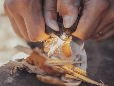 Hands carving and setting fire to small wooden sticks.