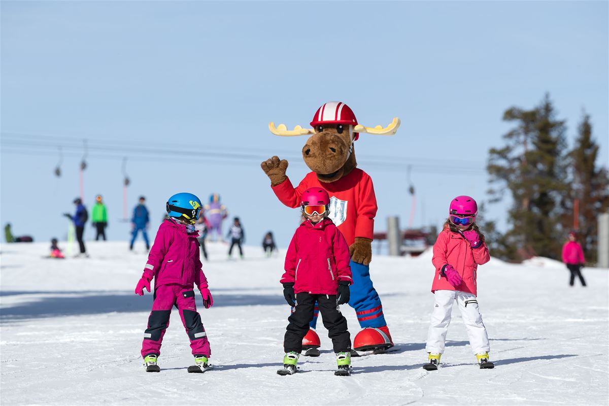 Three children in the ski slope toghether with a large stuffed toy mouse with is the mascot of Säfsen.