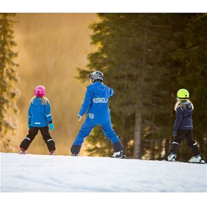 Two children skiiing together with a skiing instructor.