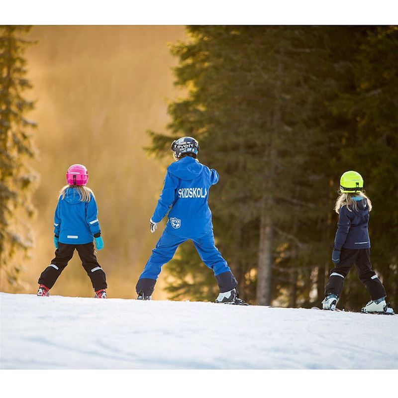 Two children skiiing together with a skiing instructor.