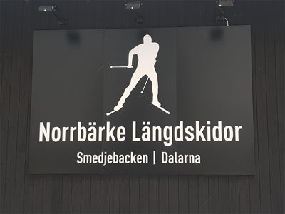 En svart anslagsskylt med texten Norrbärke längdskidor.