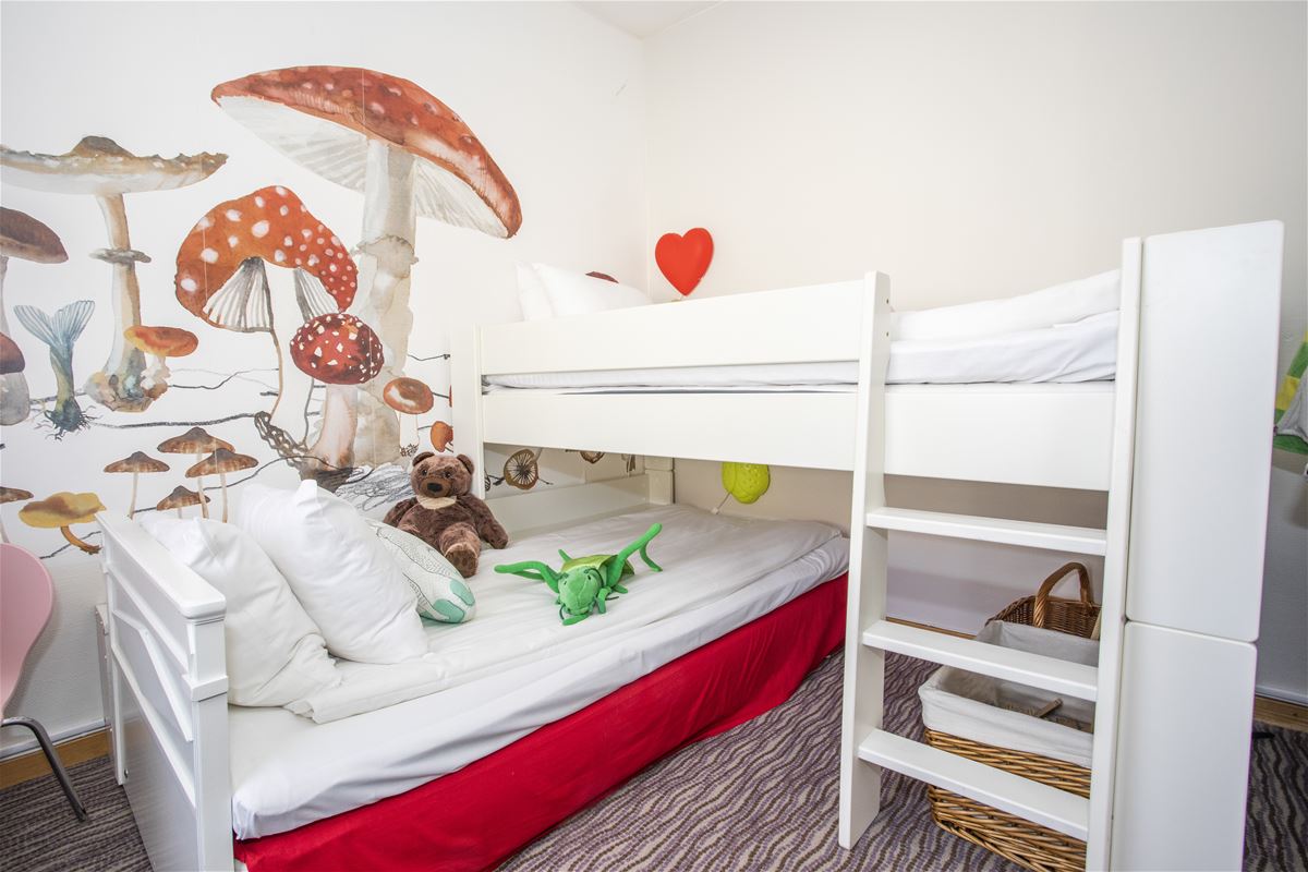 A white loft bed with a bed underneath with stuffed animals on it and painted mushrooms on the wall.